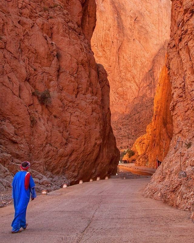 Traveler in traditional dress walking through the narrow red rock walls of Todra Gorge Morocco
